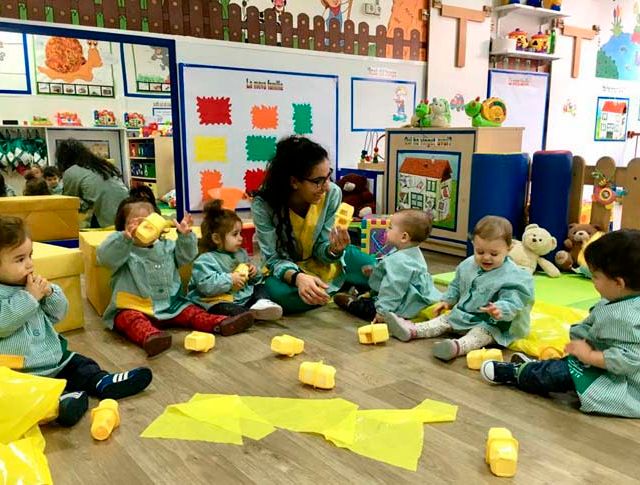  maestra y niños armando figuras con papeles amarillos